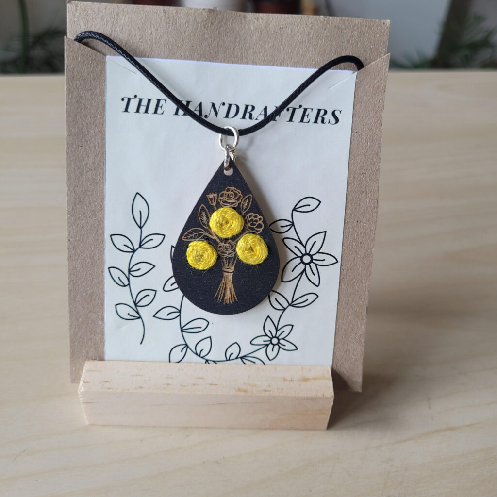 wooden teardrop shaped necklace with three embroided yellow flowers